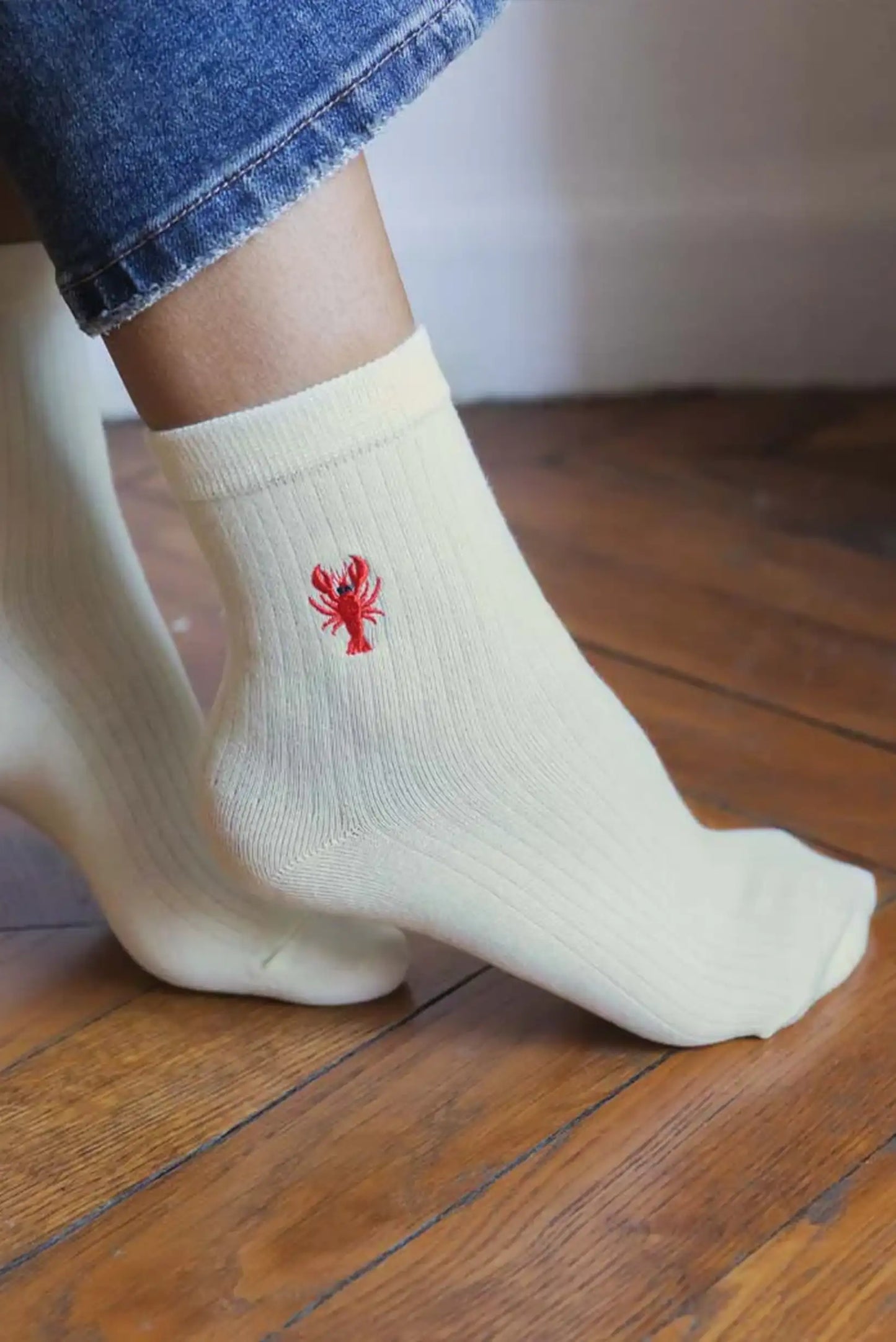 Calcetines blancos mujer con bordado de langosta roja, estilo casual sobre suelo de madera.
