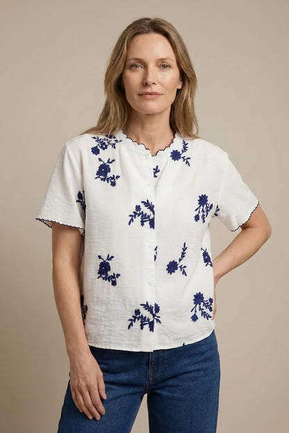 Mujer con camisa blanca de manga corta y bordado floral azul, look casual moderno.