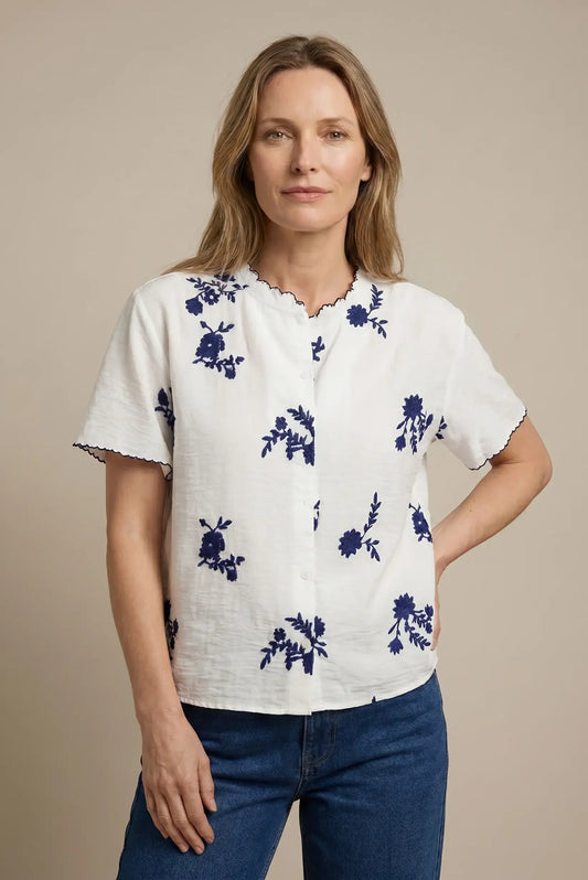 Mujer con camisa blanca de manga corta y bordado floral azul, look casual moderno.