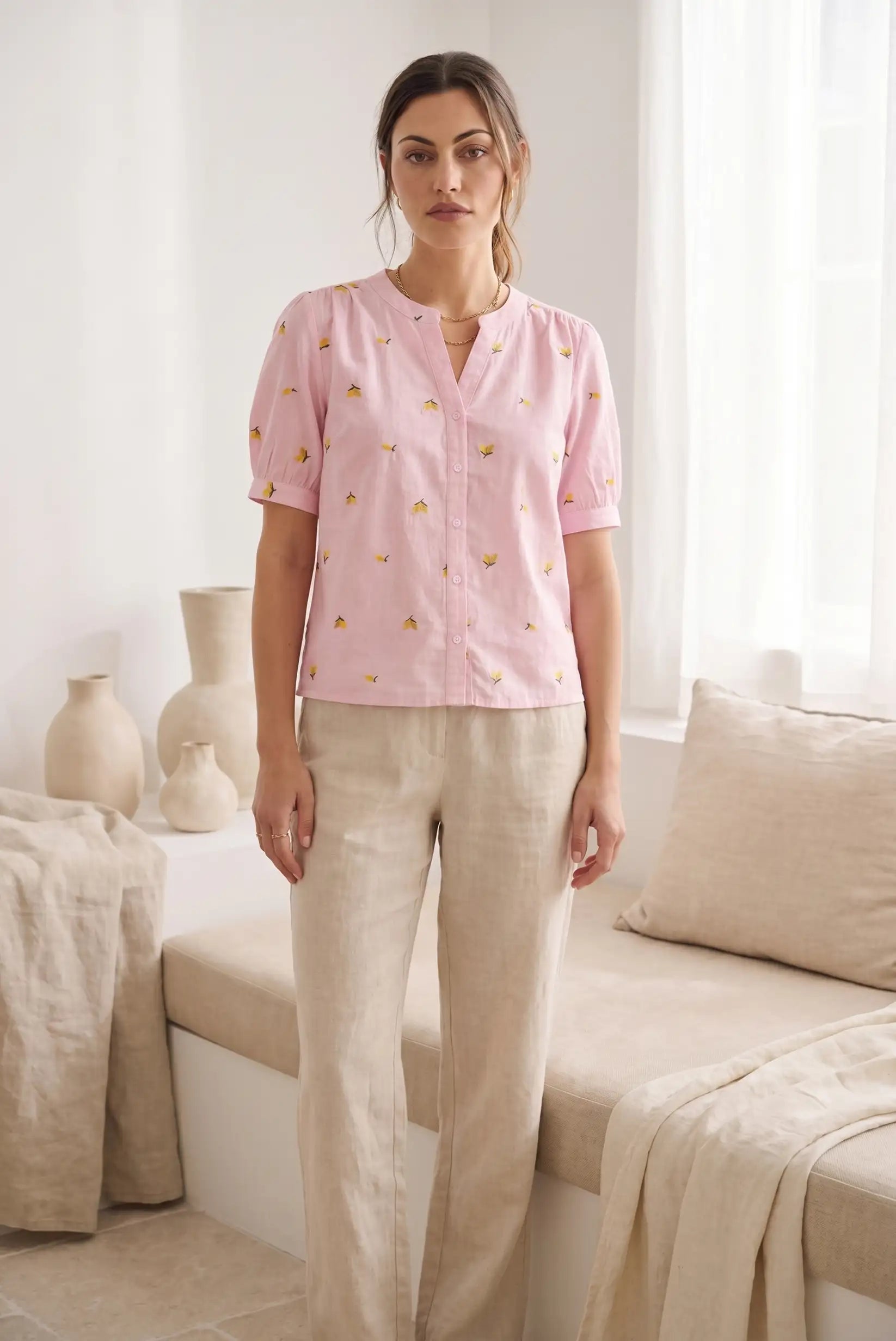 Mujer con camisa rosa de manga corta con estampado de limones y pantalón beige, en ambiente minimalista