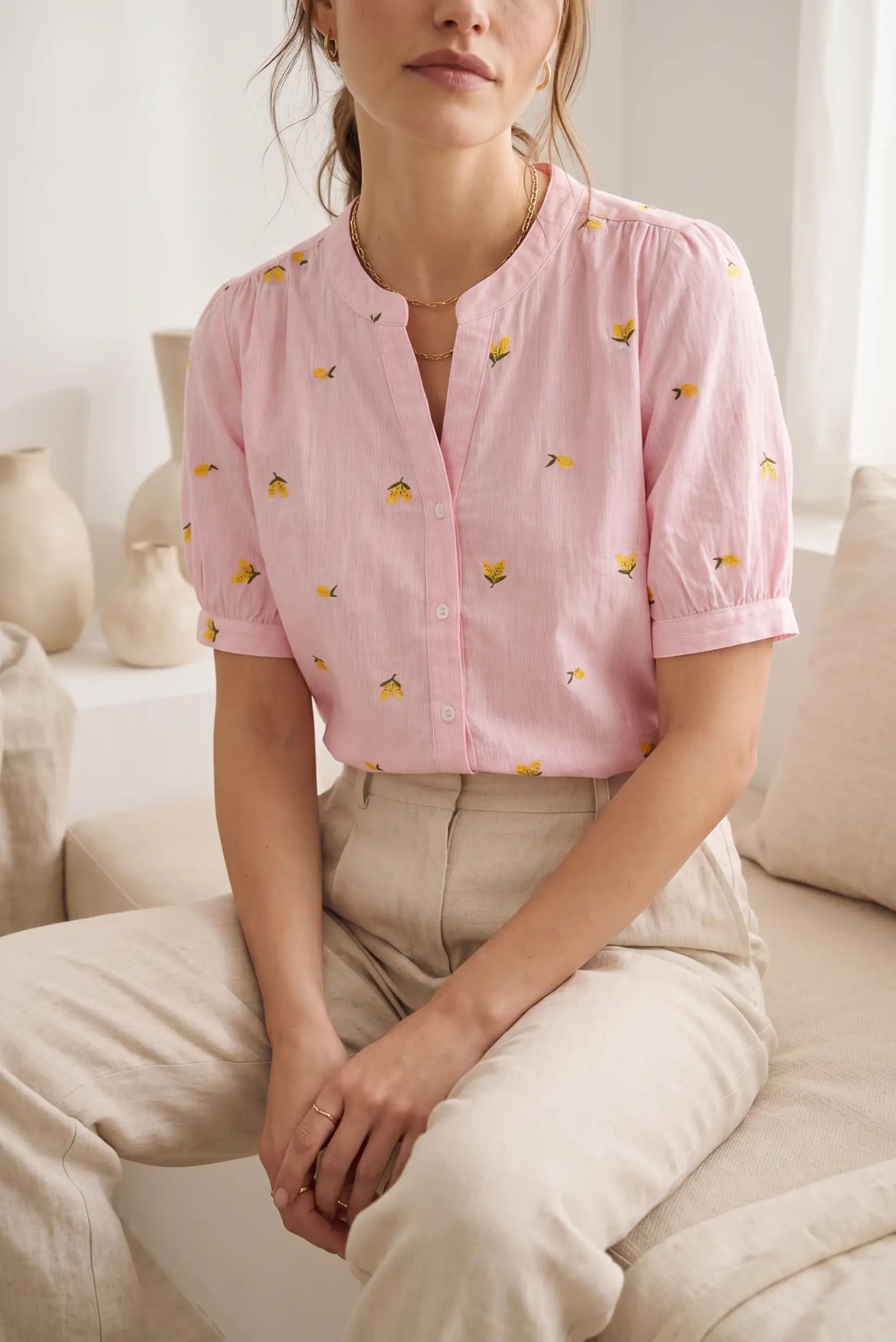 Mujer con blusa rosa de manga corta con limones bordados y pantalón beige, look casual femenino.