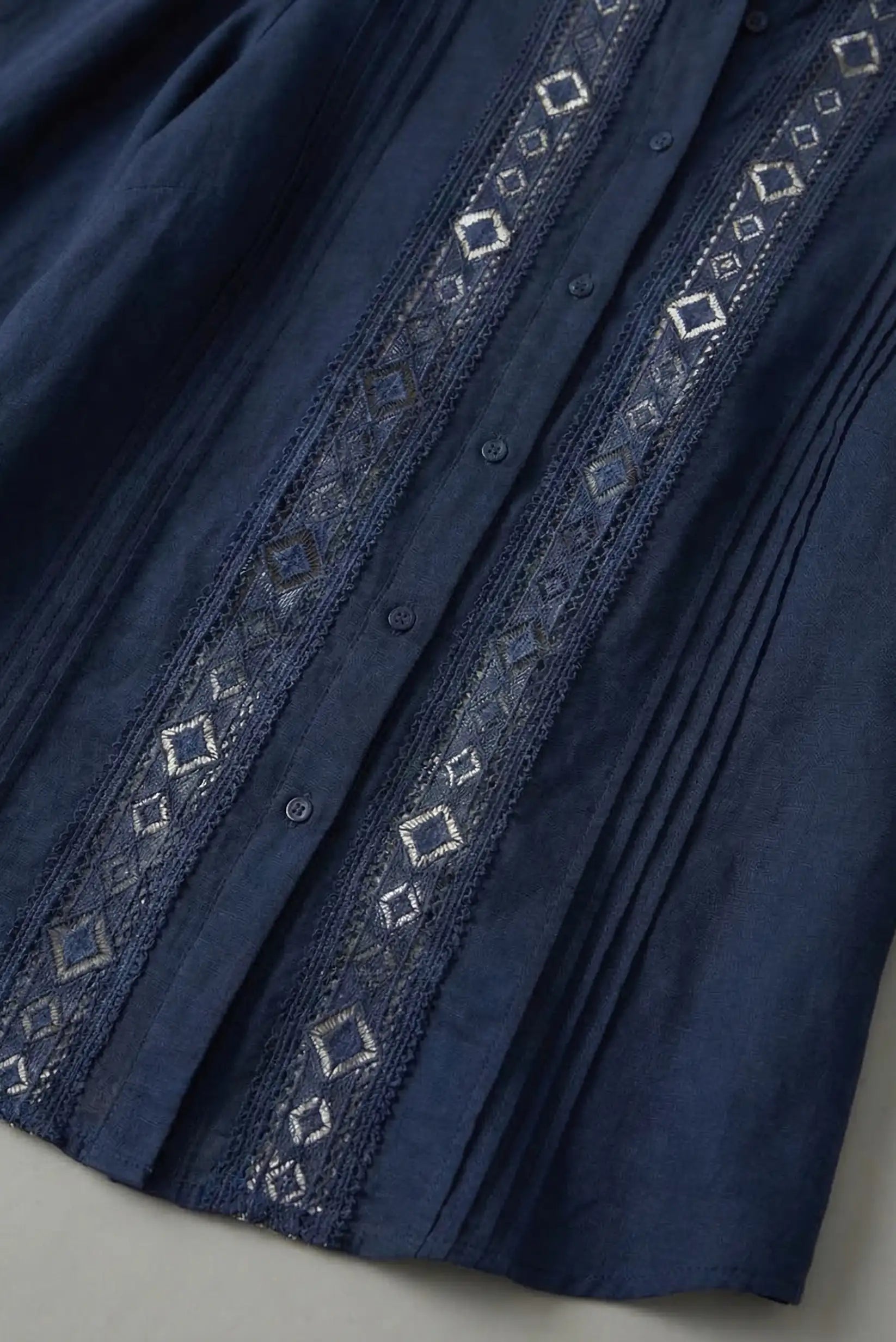 Detalle de camisa azul de manga larga con bordados geométricos en el frente, moda femenina