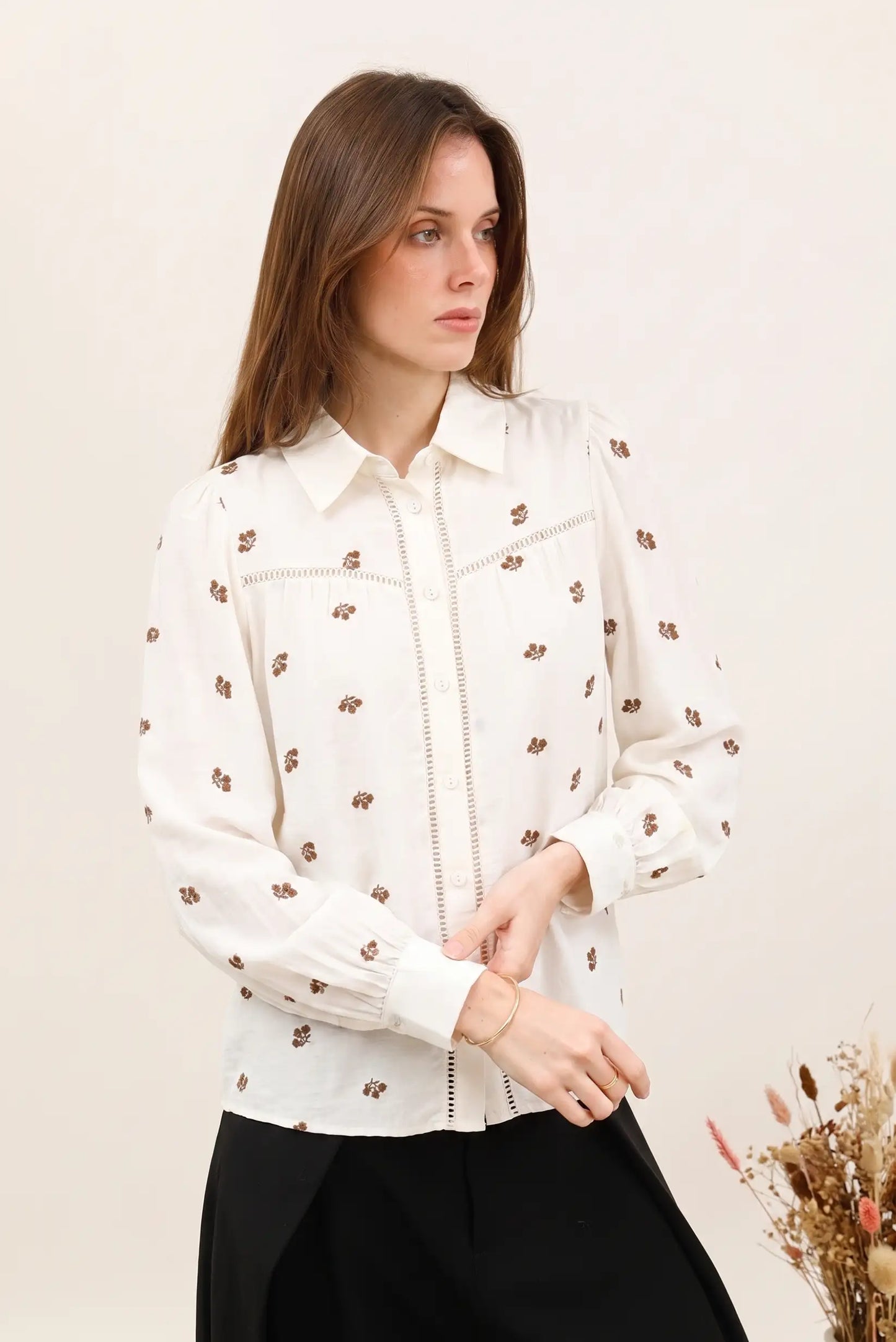Camisa blanca con estampado floral marrón, cuello clásico y detalles bordados, ideal para looks femeninos y elegantes.