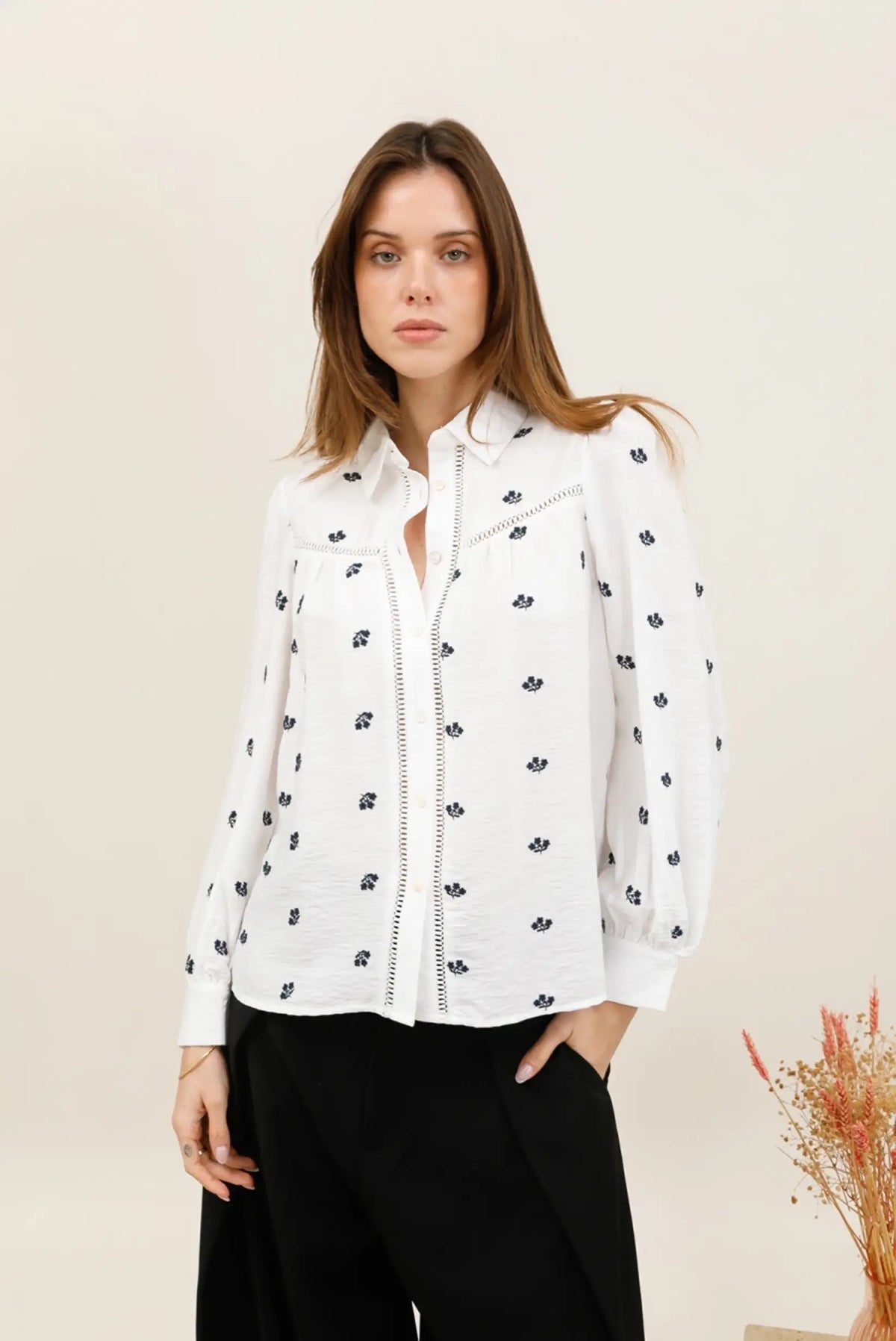 Mujer vistiendo blusa blanca con estampado floral azul y pantalones negros.