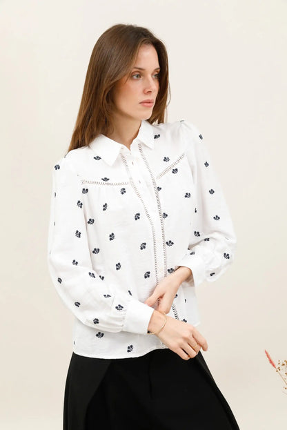 Mujer joven vistiendo una camisa blanca con estampado floral azul y detalles de encaje.