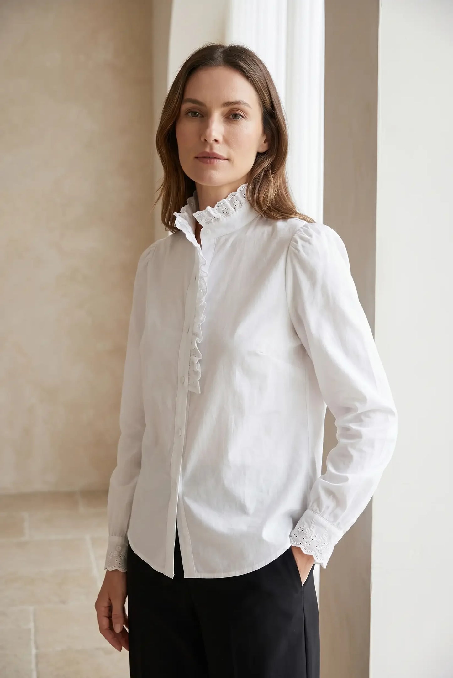 Mujer con camisa blanca de manga larga, volantes en el cuello y puños calados, estilo elegante.