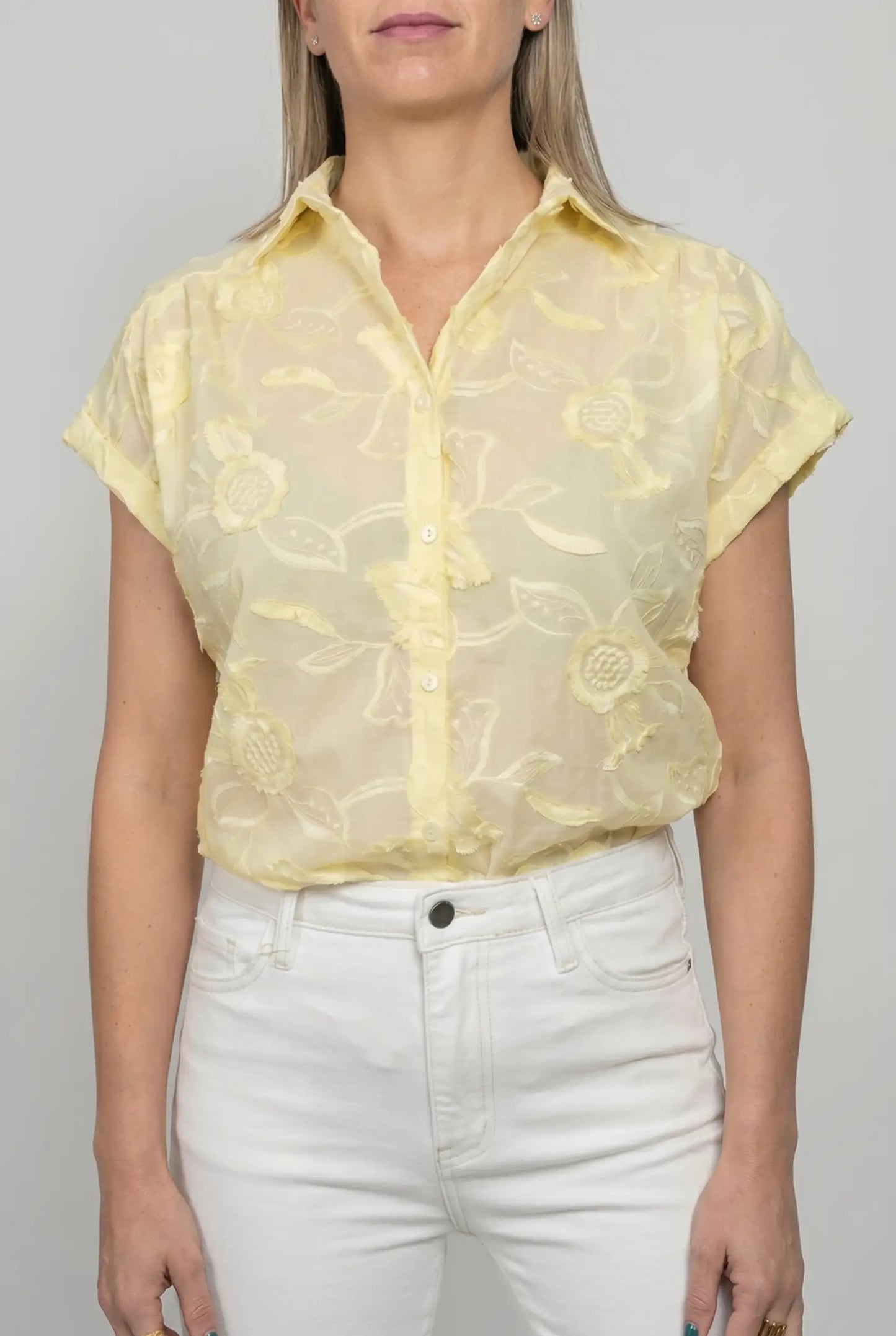 Mujer con camisa amarilla de manga corta y bordado floral, combinada con pantalón blanco