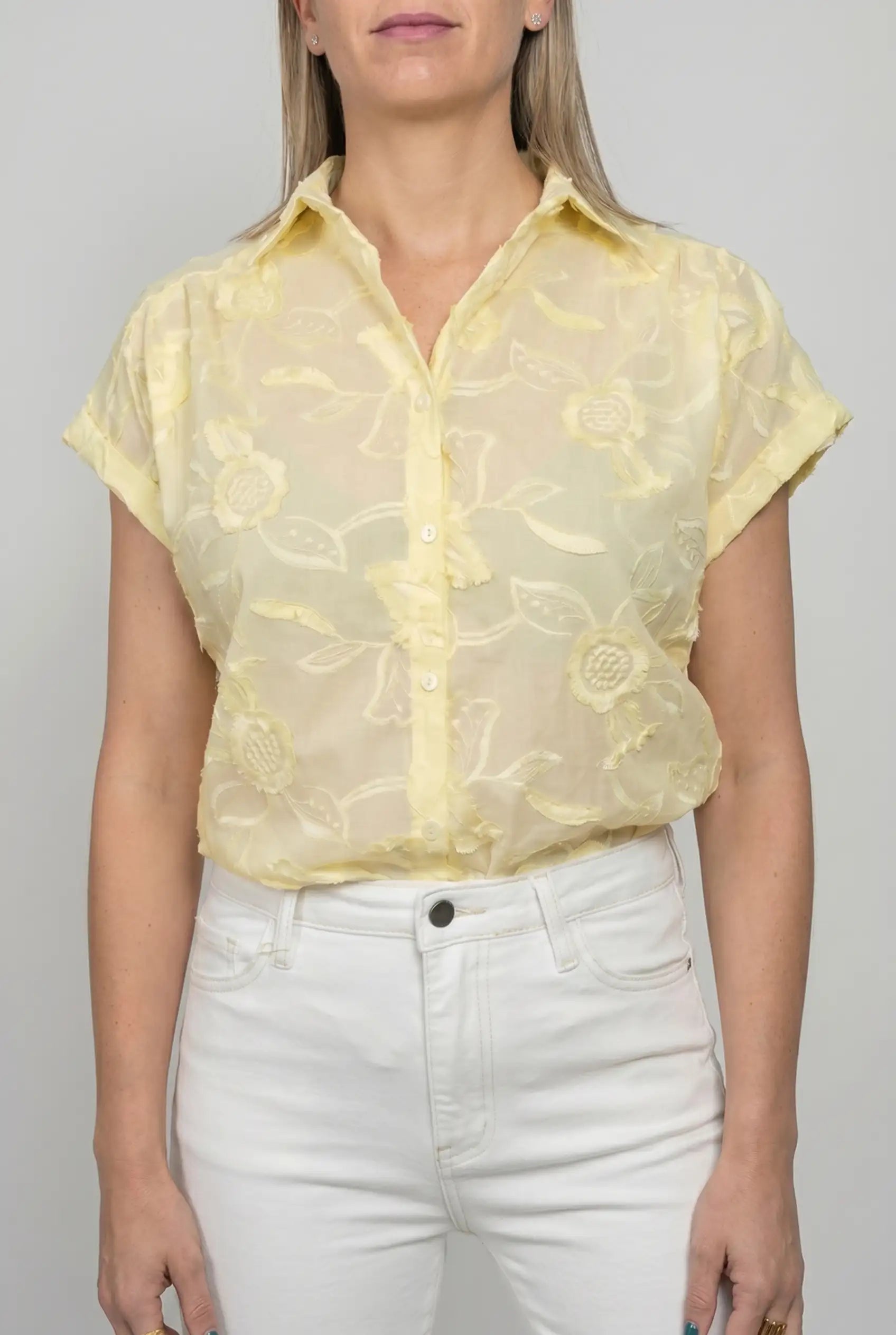 Mujer con camisa amarilla de manga corta y bordado floral, combinada con pantalón blanco