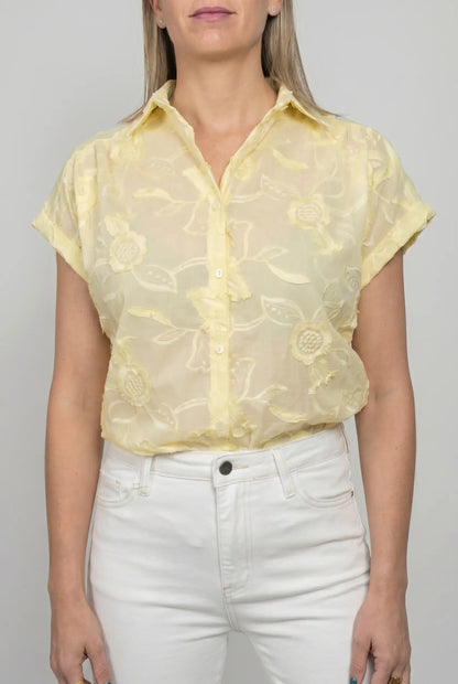 Mujer con camisa amarilla de manga corta y bordado floral, combinada con pantalón blanco