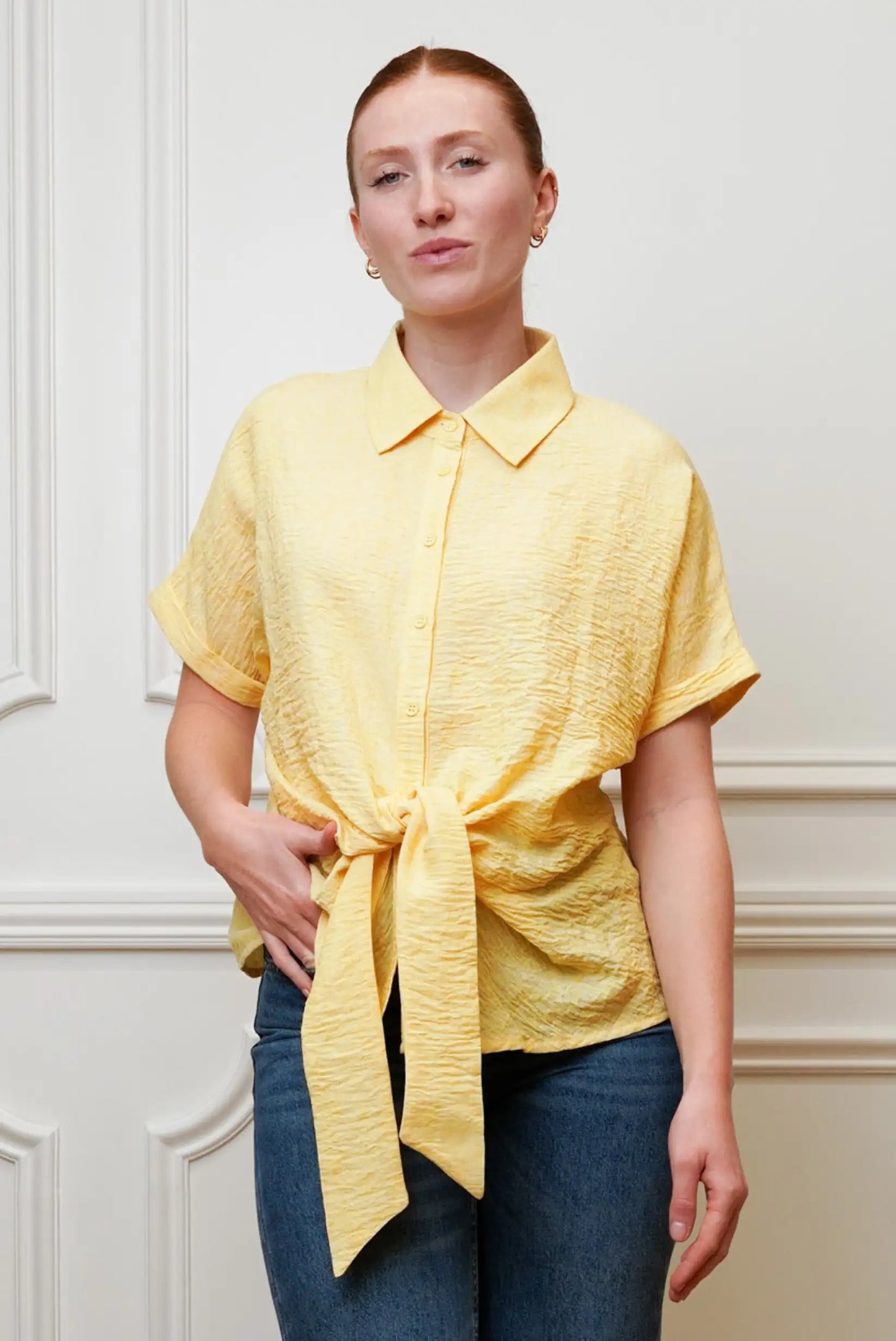 Mujer con camisa amarilla pastel de manga corta, nudo frontal y jeans, moda primavera casual.