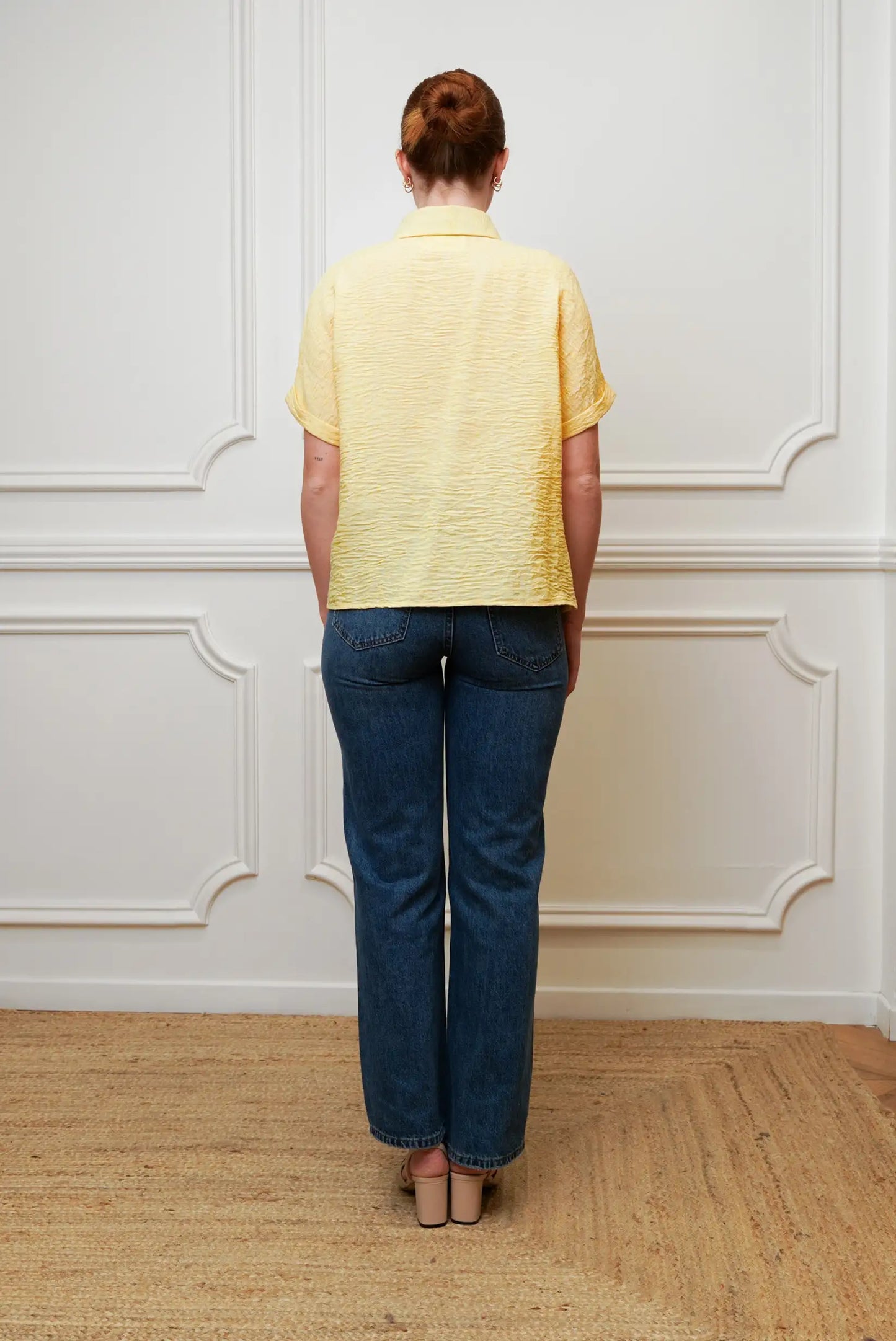 Mujer de espaldas con camisa amarilla pastel de manga corta y jeans azules