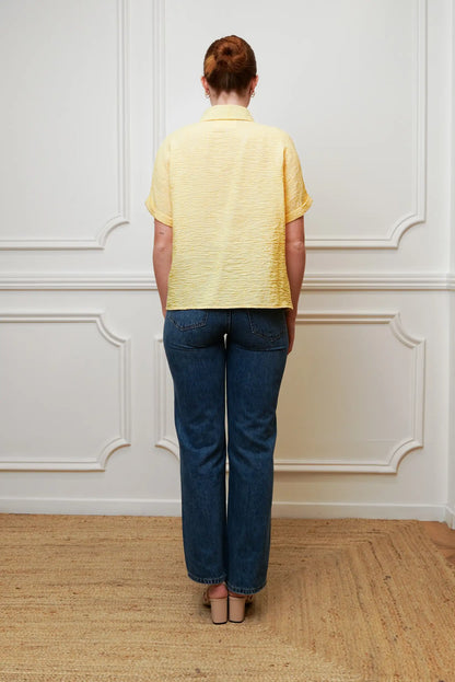Mujer de espaldas con camisa amarilla pastel de manga corta y jeans azules