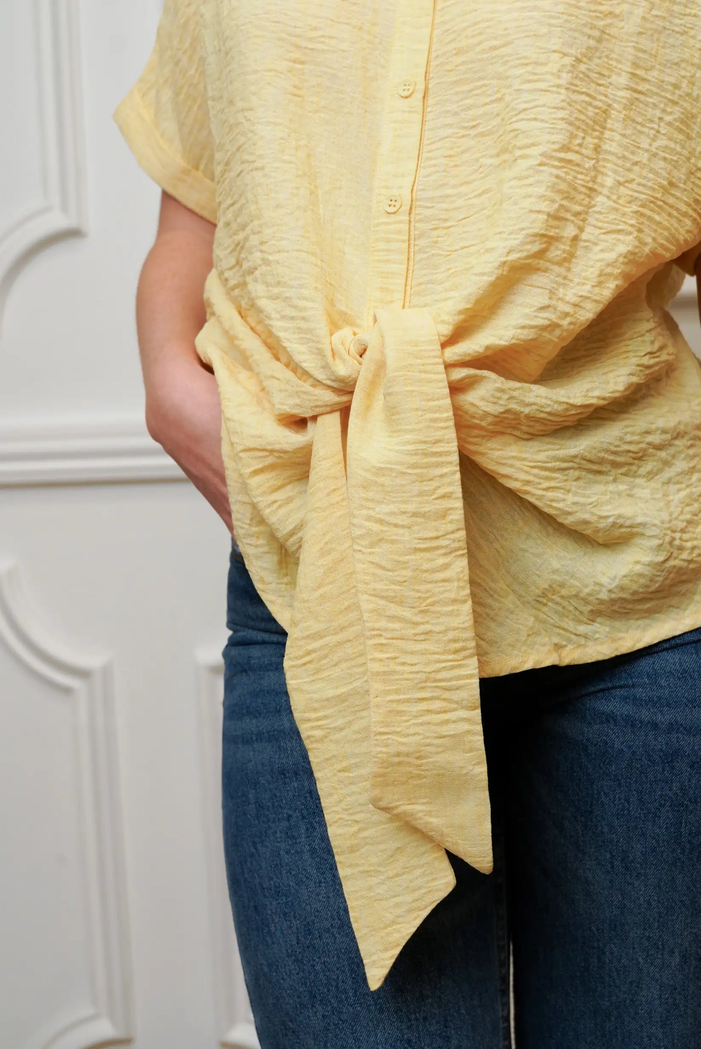 Camisa de mujer amarilla pastel con lazo delantero, textura arrugada y jeans azul