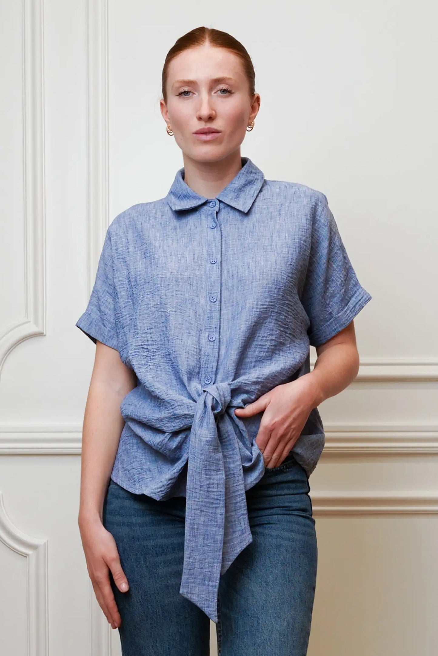 Mujer con camisa azul de manga corta anudada, estilo casual primaveral, combinada con jeans.