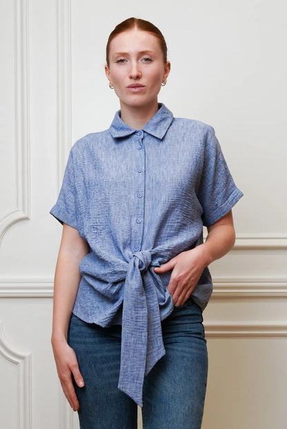 Mujer con camisa azul de manga corta anudada, estilo casual primaveral, combinada con jeans.