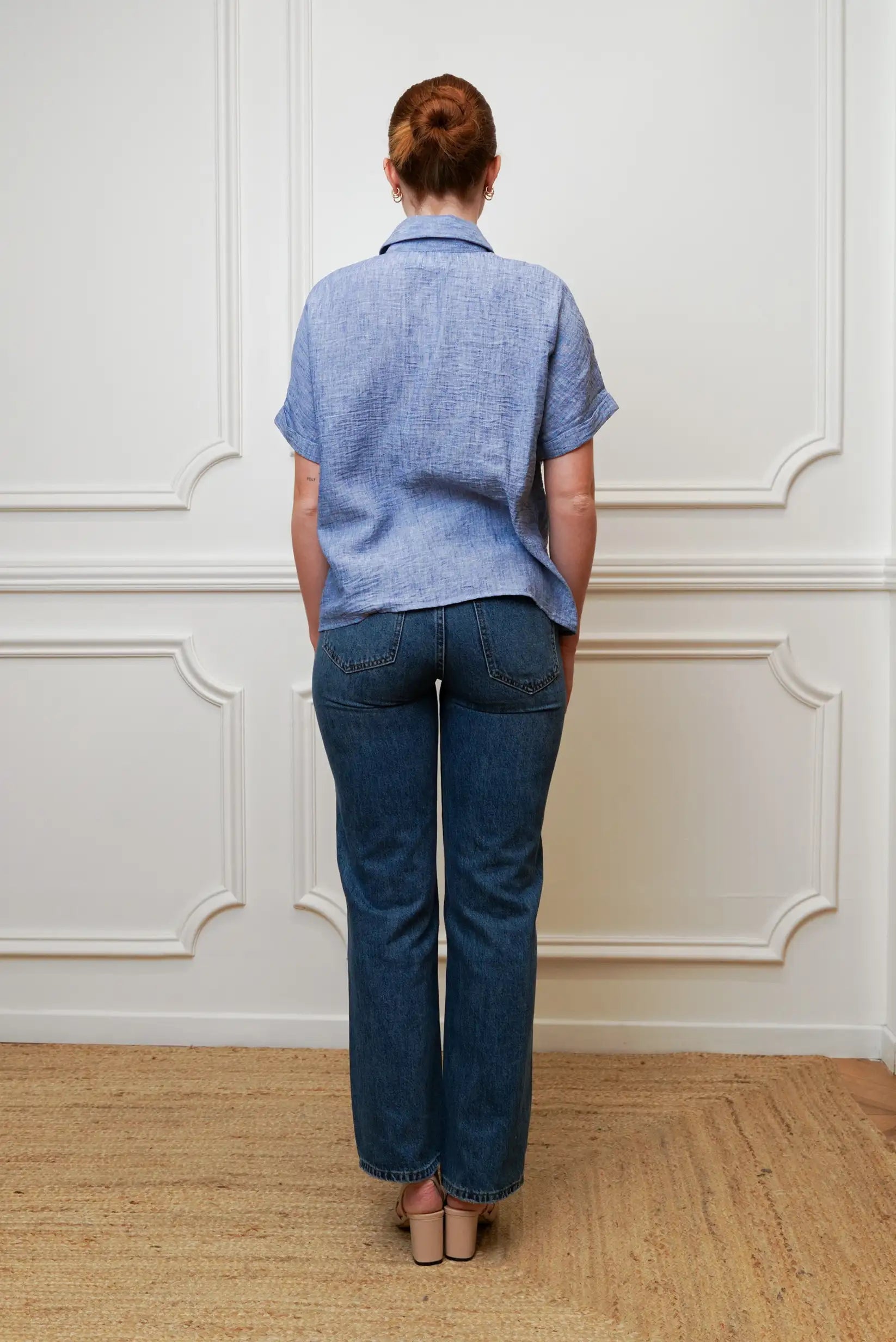 Mujer de espaldas con camisa azul de manga corta y jeans rectos, look casual primavera.