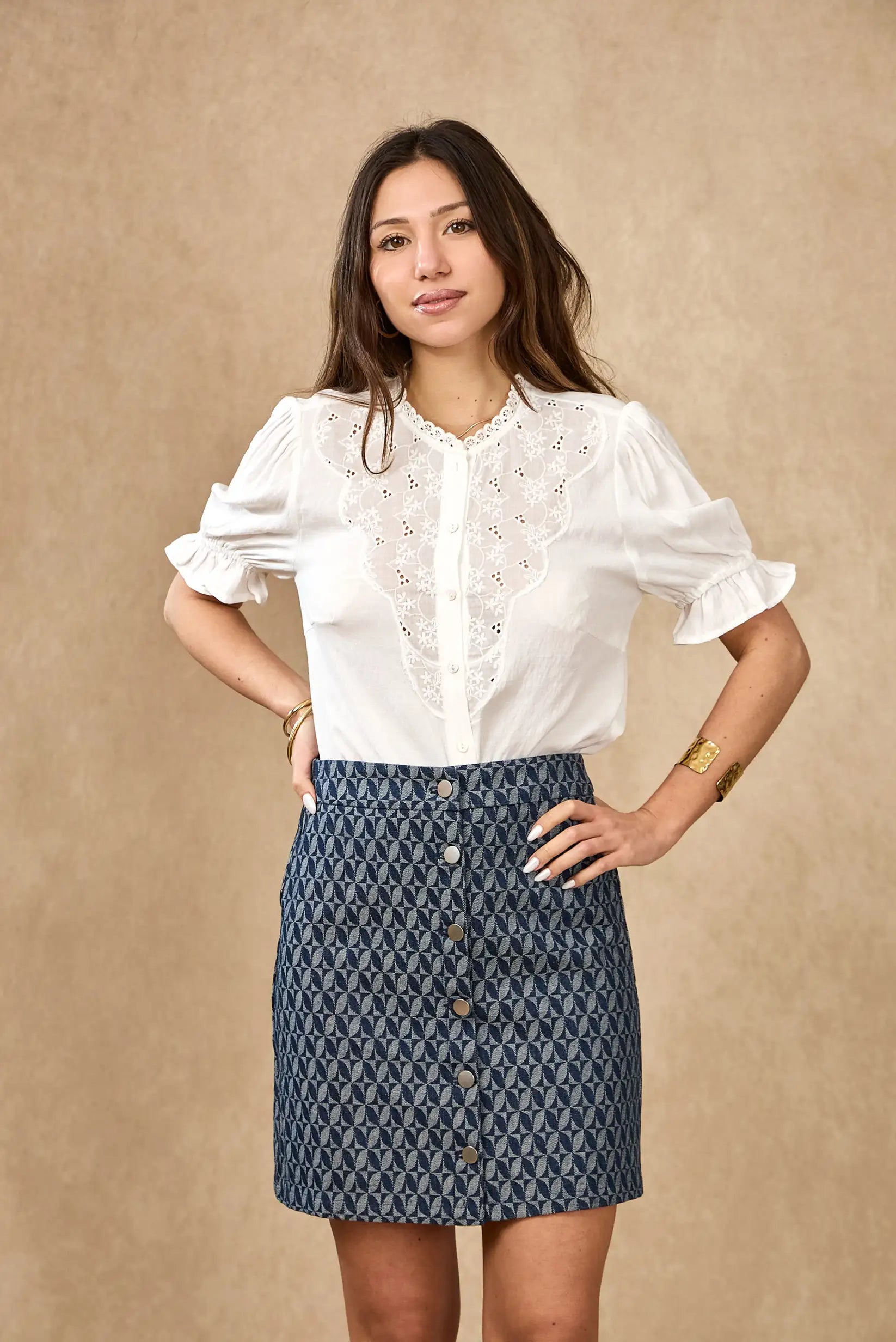 Mujer con camisa blanca bordada de manga corta y falda azul estampada, moda primavera casual.