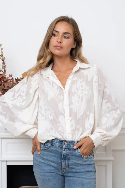 Mujer con blusa blanca roto manga larga con estampado floral y jeans azules claros