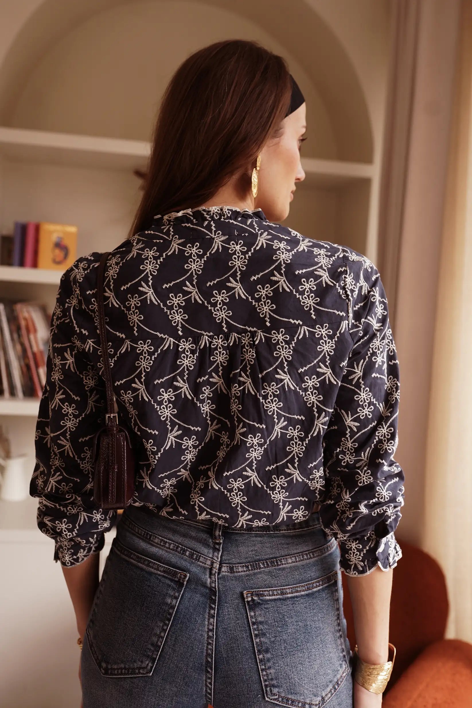 Blusa negra con estampado floral blanco, jeans y accesorios dorados para mujer