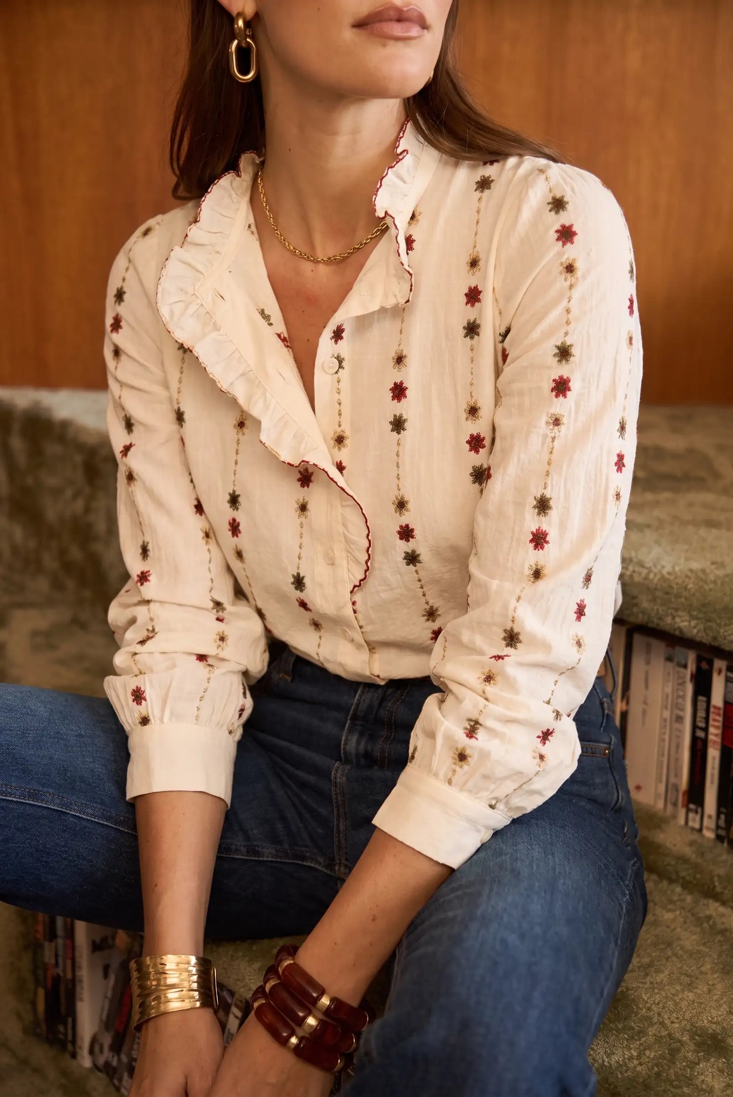 Blusa blanca con bordado floral y volantes, combinada con jeans y joyas doradas, estilo boho chic.