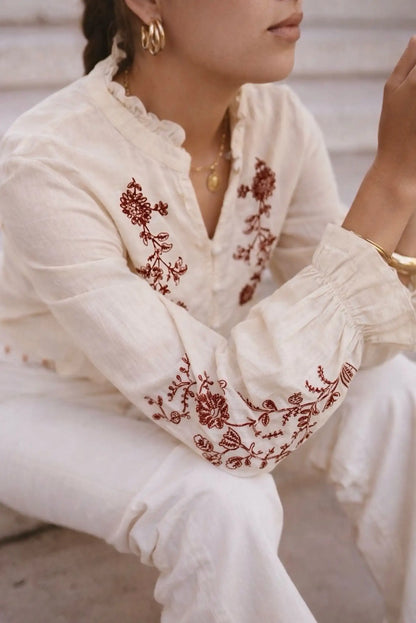 Blusa blanca con bordado floral rojo, mangas abullonadas y cuello fruncido, ideal para looks boho y elegantes.
