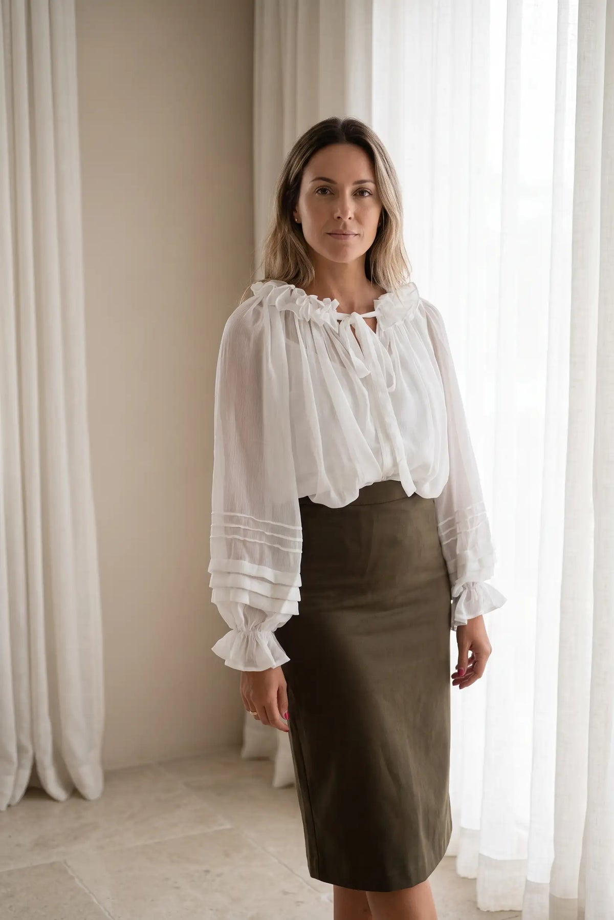 Mujer con blusa blanca romántica de volantes y falda midi en color verde oliva.