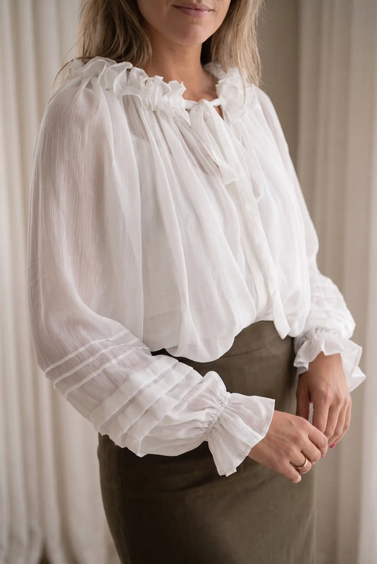 Blusa blanca vaporosa con cuello de volantes y puños fruncidos combinada con falda verde oliva.