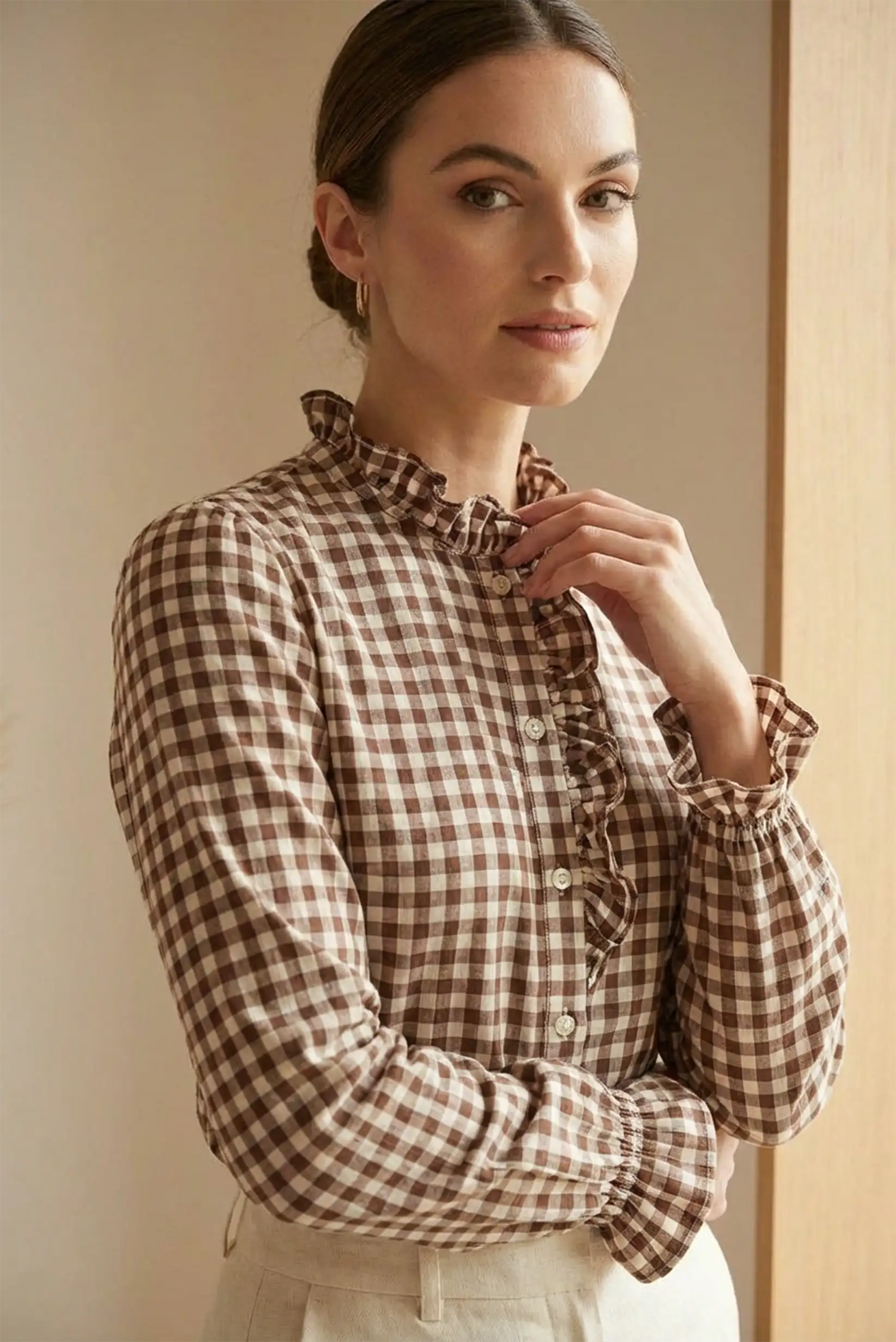 Mujer con blusa de manga larga de cuadros marrones con volantes en cuello y puños, fondo neutro