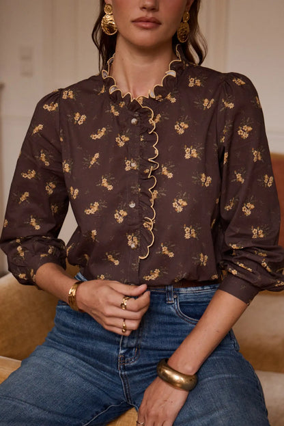 Blusa marrón con estampado floral y detalles de volantes, combinada con jeans y accesorios dorados