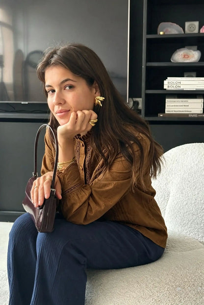 Mujer con blusa marrón de encaje, pantalones azules y bolso pequeño. Moda femenina elegante y cómoda.