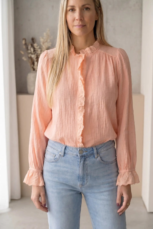 Mujer con camisa de manga larga salmón con volantes y jeans claros, moda casual primavera.