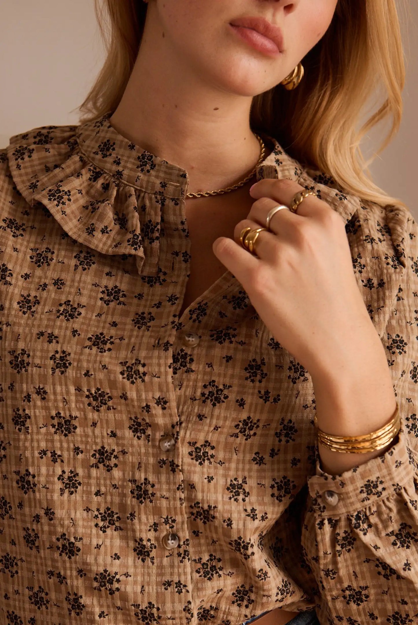 Blusa femenina con estampado floral y detalles de volantes, ideal para looks de moda con accesorios dorados.