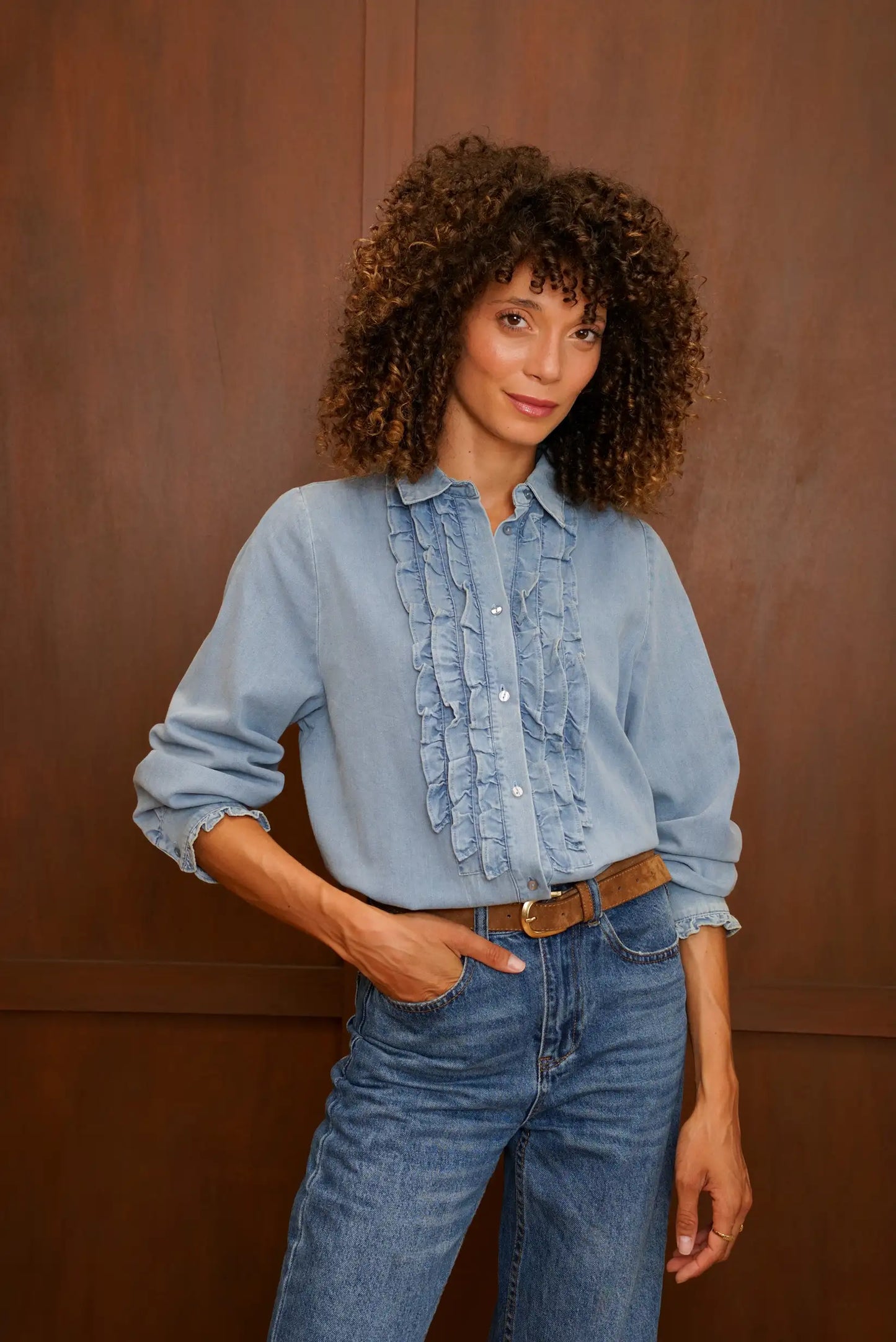 Mujer con camisa vaquera azul con volantes frontales y pantalones vaqueros.