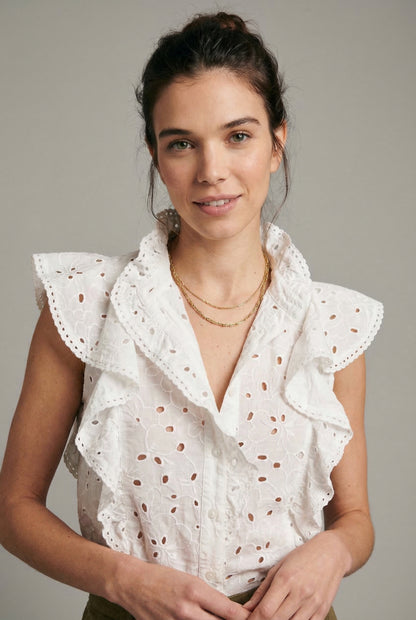 Mujer con blusa blanca sin mangas, volantes y bordado floral, estilo primavera casual.