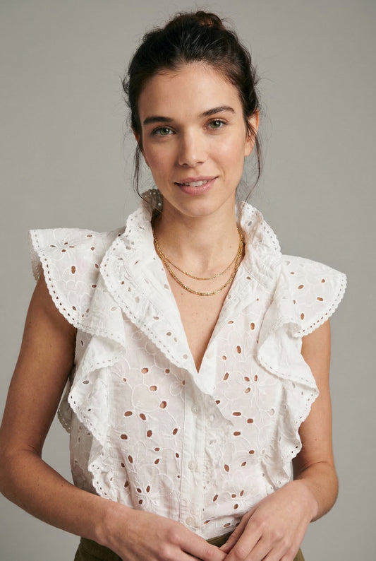 Mujer con blusa blanca sin mangas, volantes y bordado floral, estilo primavera casual.