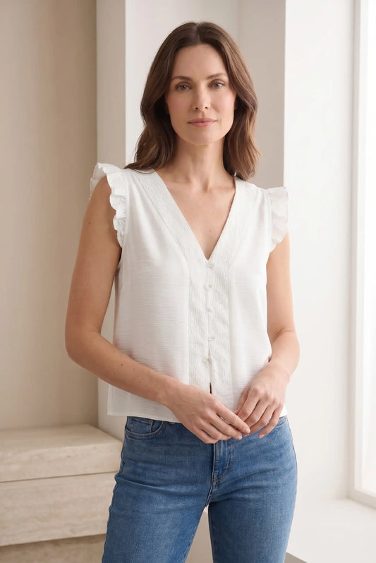 Mujer con blusa blanca sin mangas, cuello en V y botones, combinada con vaqueros azules