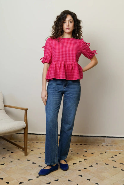Mujer con blusa rosa de cuadros, manga corta y lazos, jeans azules y zapatos planos.
