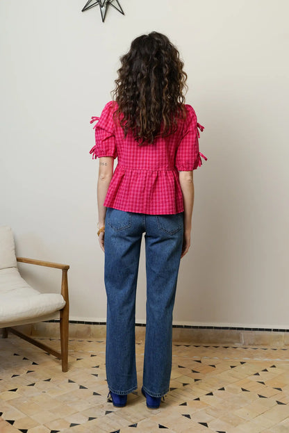 Mujer de espaldas con camisa rosa de cuadros y manga corta, pantalón vaquero recto.