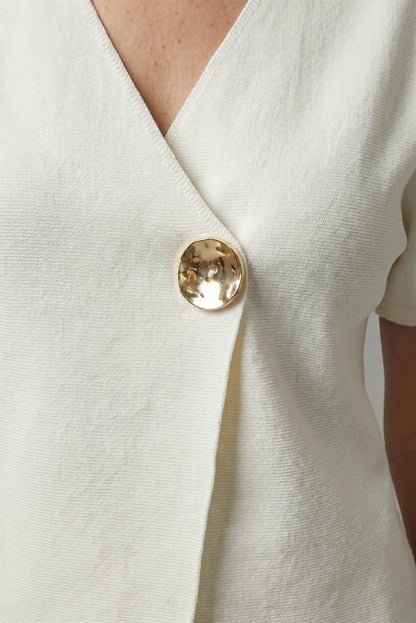 Detalle de camisa blanca de mujer cruzada con botón dorado grande, estilo casual