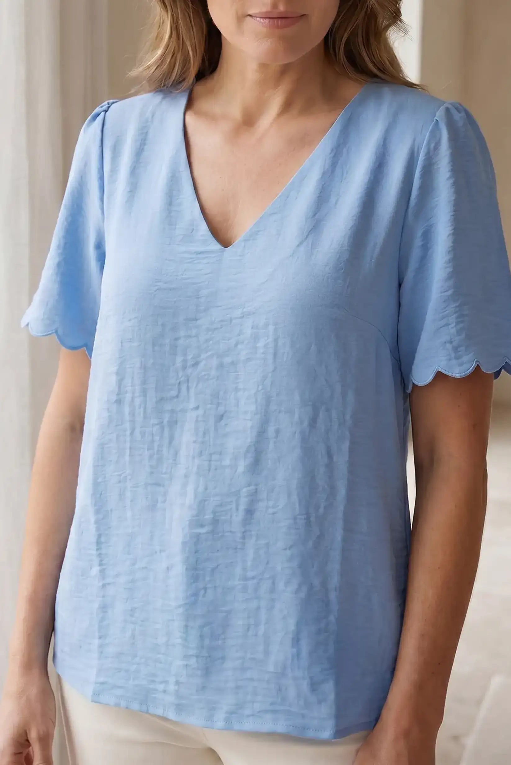 Blusa azul claro con cuello en V y mangas cortas con detalle ondulado, ideal para looks casuales y estilosos.