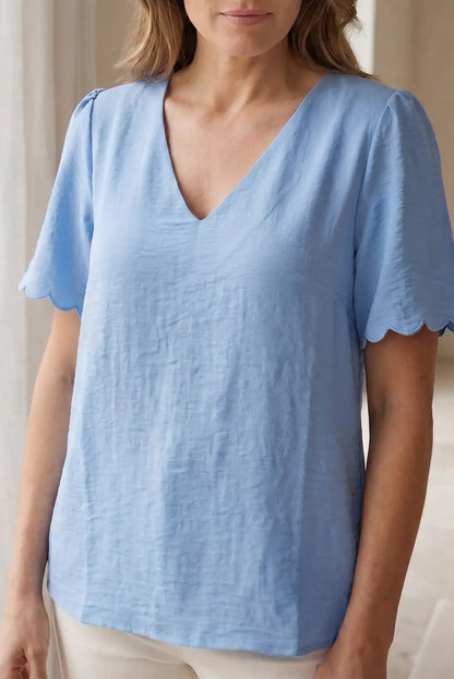 Blusa azul claro con cuello en V y mangas cortas con detalle ondulado, ideal para looks casuales y estilosos.