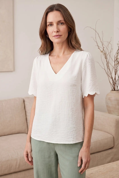 Blusa blanca con cuello en V y mangas cortas con detalle de volante, ideal para looks casuales y estilosos.