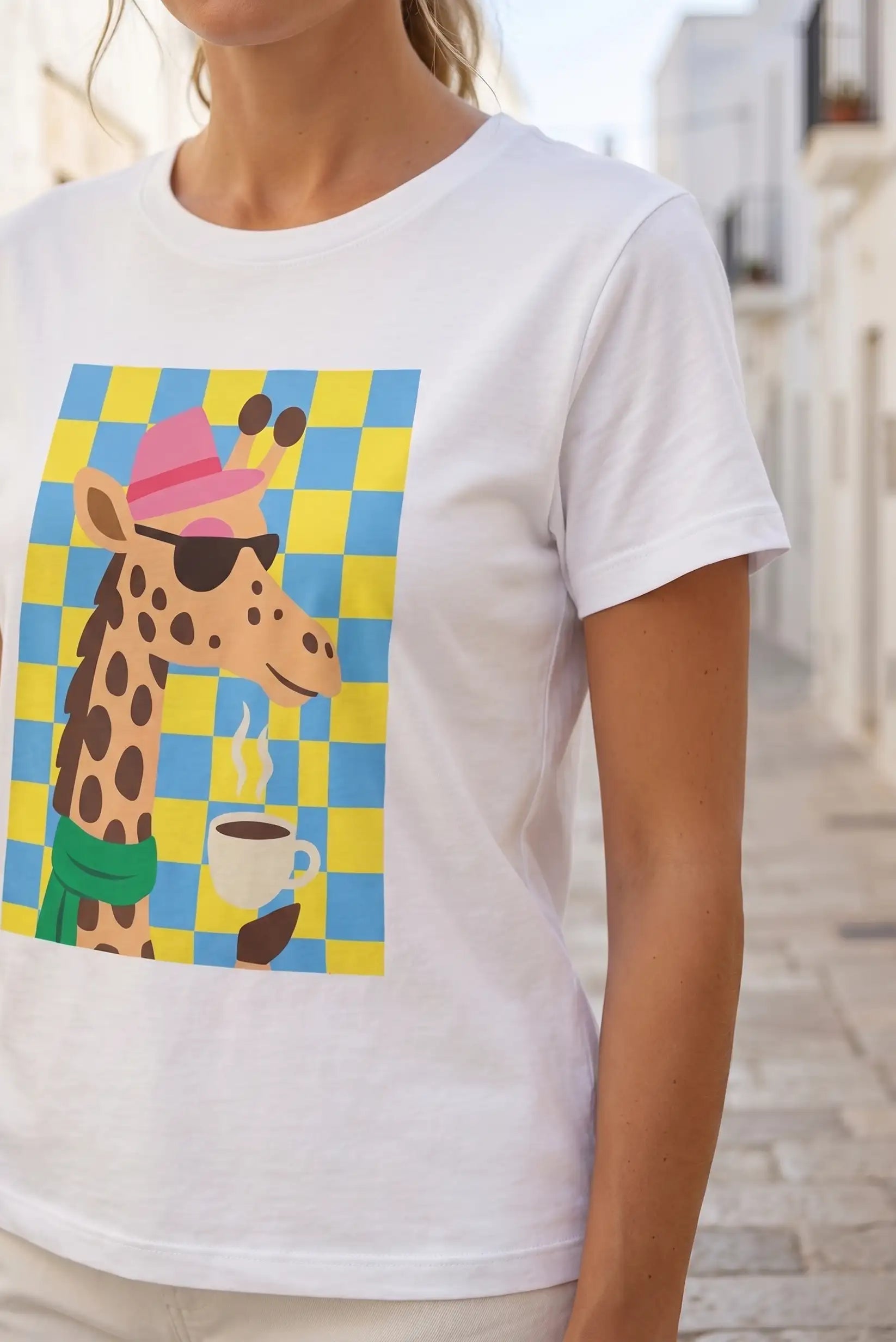 Camiseta blanca con jirafa estilizada, sombrero rosa, gafas y taza de café sobre fondo a cuadros