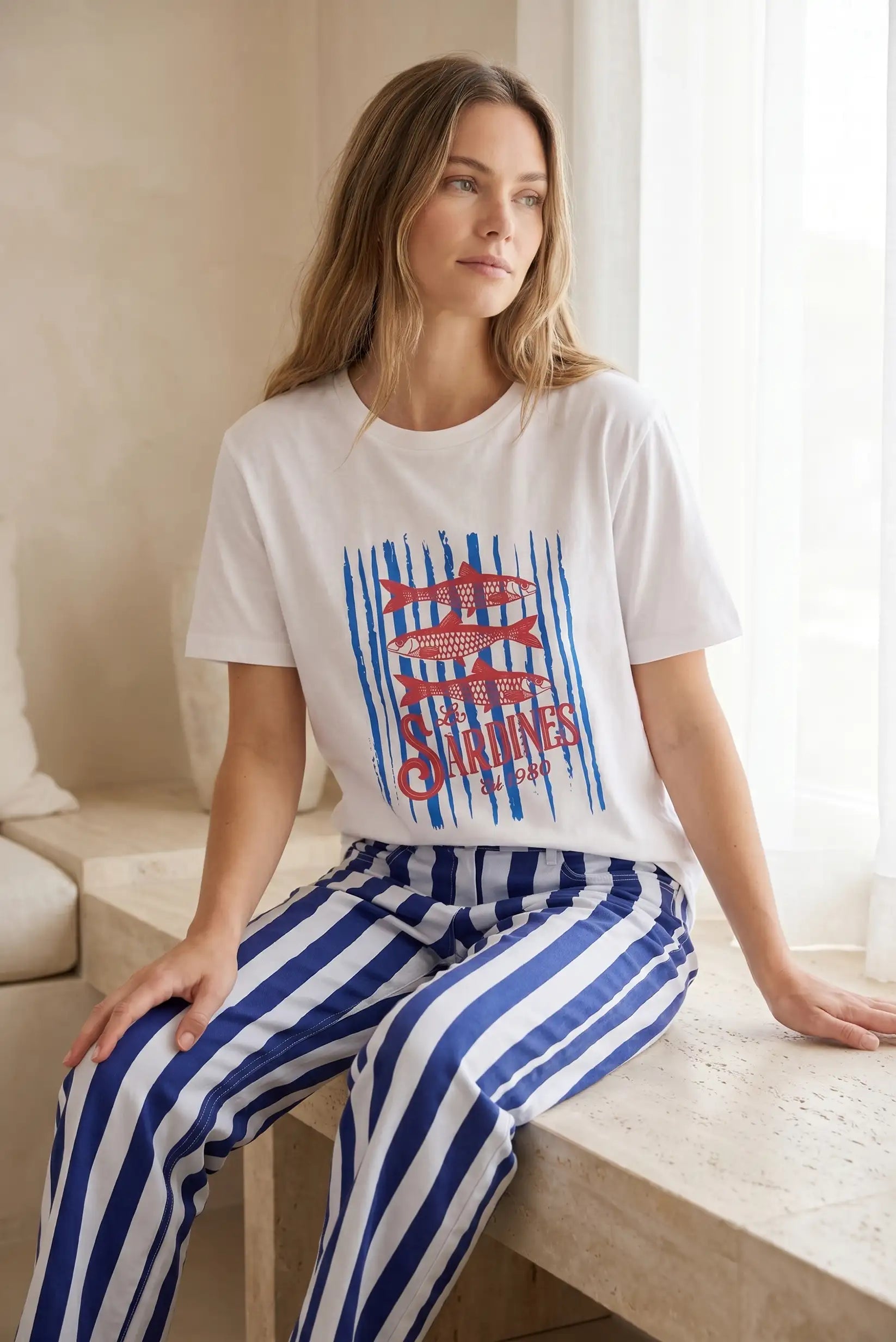 Mujer con camiseta blanca de manga corta con estampado de sardinas rojas y pantalón a rayas azules.