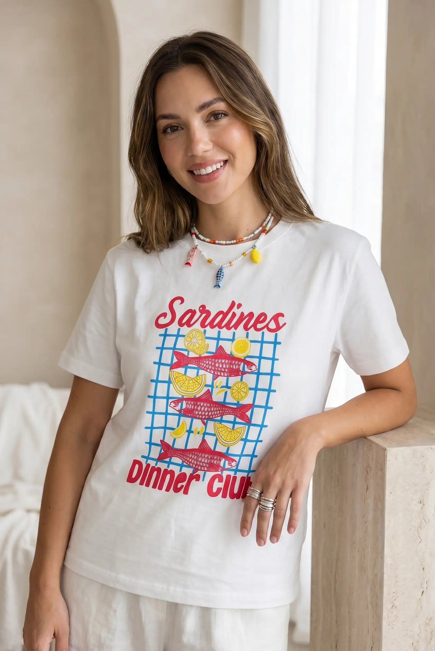 Mujer con camiseta blanca de manga corta estampada con sardinas rojas y limones amarillos, estilo casual.