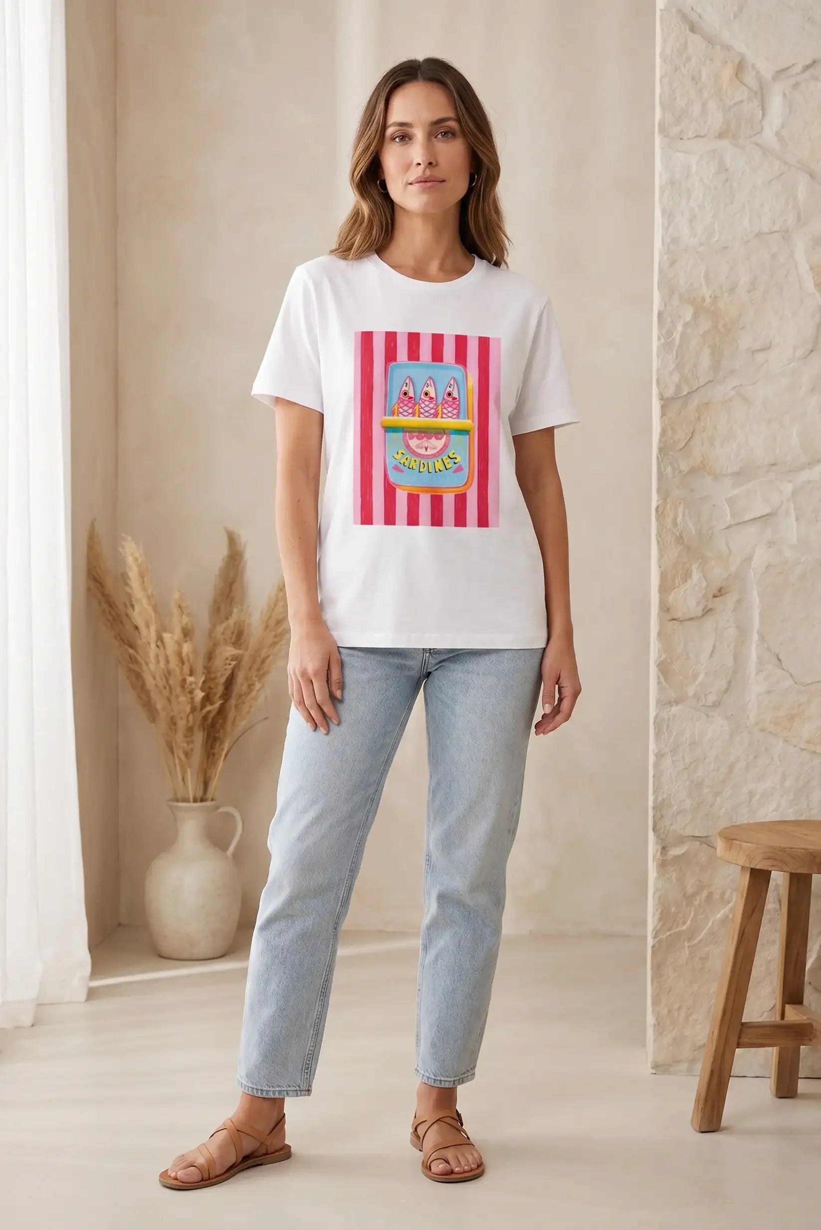 Mujer con camiseta blanca de manga corta con estampado colorido de sardinas, jeans claros y sandalias, en ambiente casual.