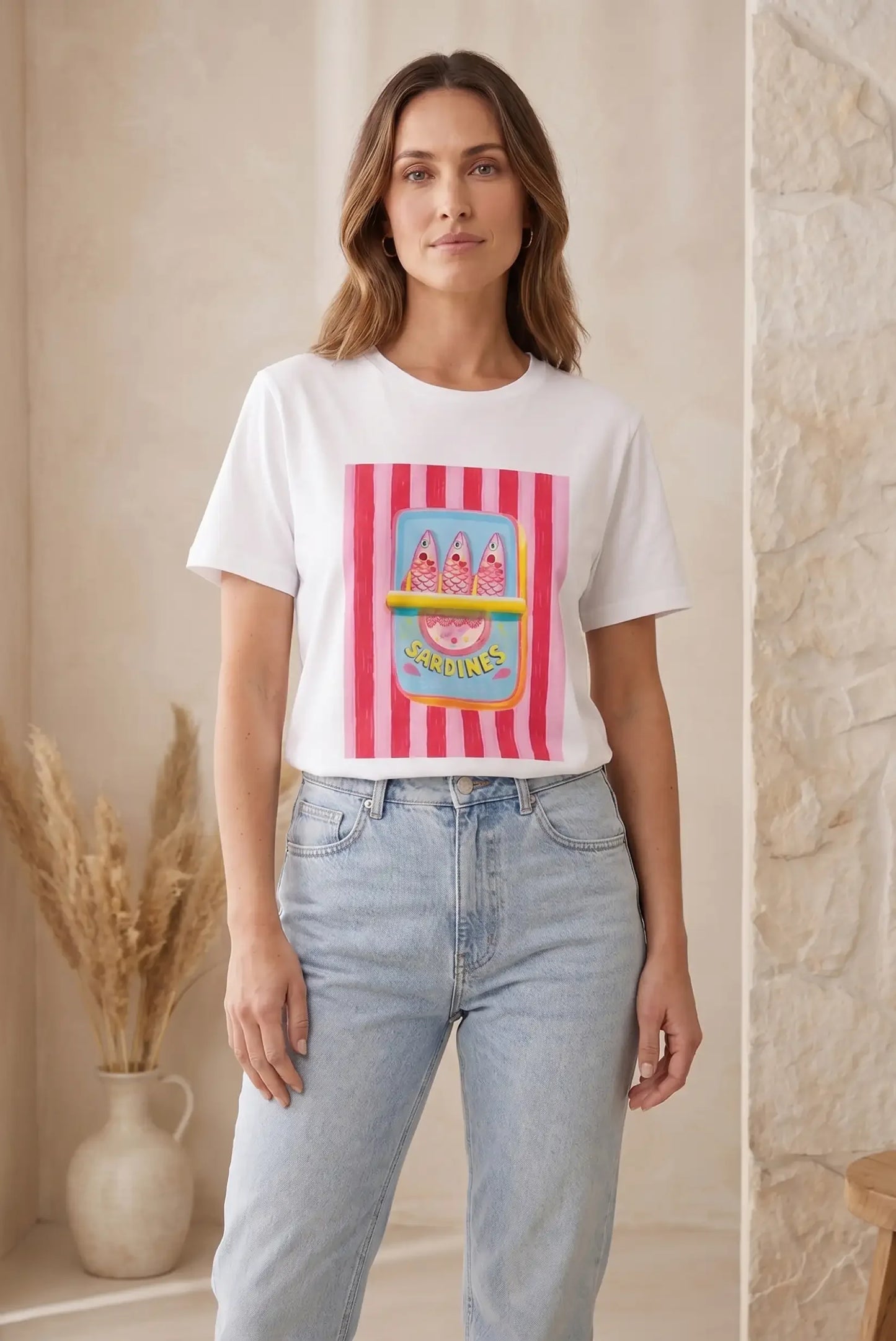 Mujer con camiseta blanca de manga corta, diseño de sardinas rosas, y vaqueros claros.