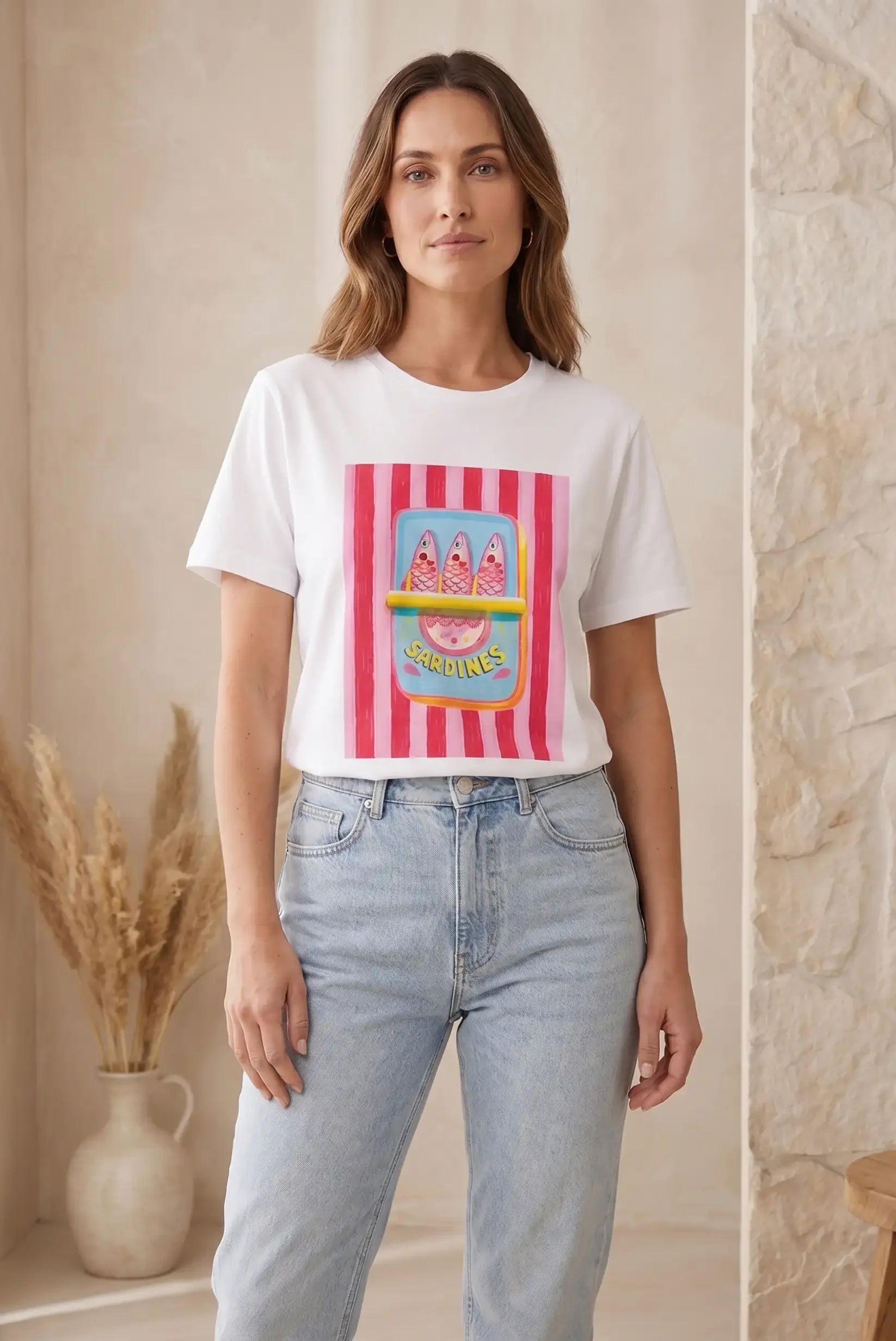 Mujer con camiseta blanca de manga corta, diseño de sardinas rosas, y vaqueros claros.