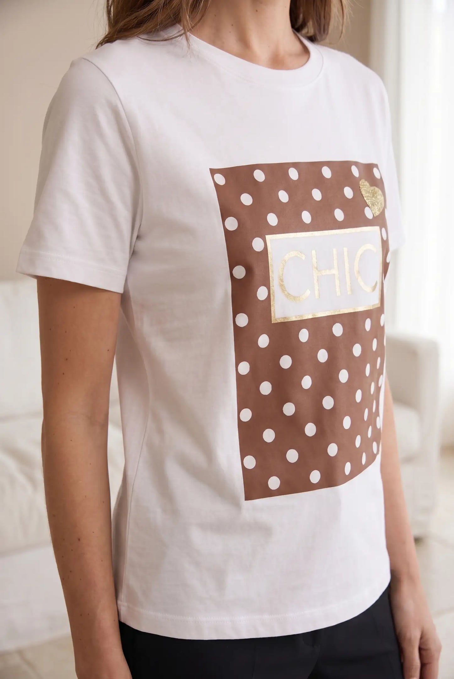 Camiseta blanca de mujer con mangas cortas, estampado marrón de lunares y texto CHIC dorado.