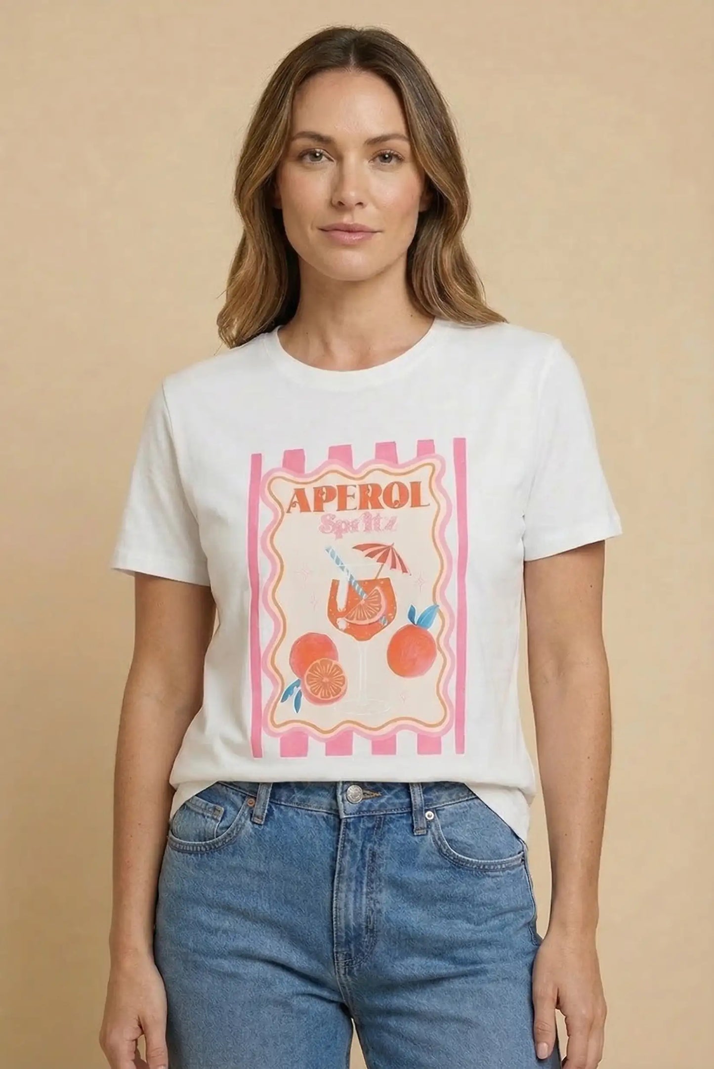 Mujer con camiseta blanca de manga corta, estampado Aperol Spritz y jeans azules casual.